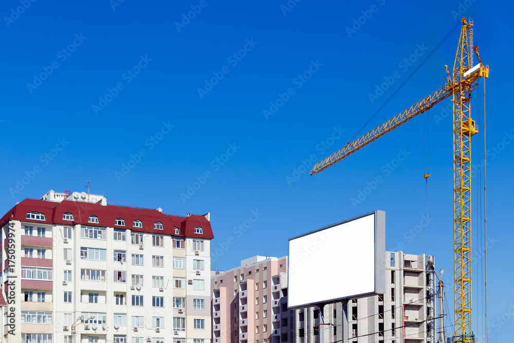 Building crane against the background of a multi-storey building under construction. Advertising billboard with copy space.
