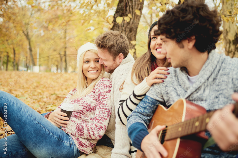      Friends having a good time in park at autumn/ singing and playing guitar 
