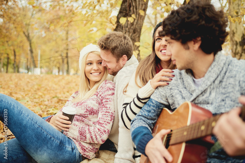  Friends having a good time in park at autumn/ singing and playing guitar 