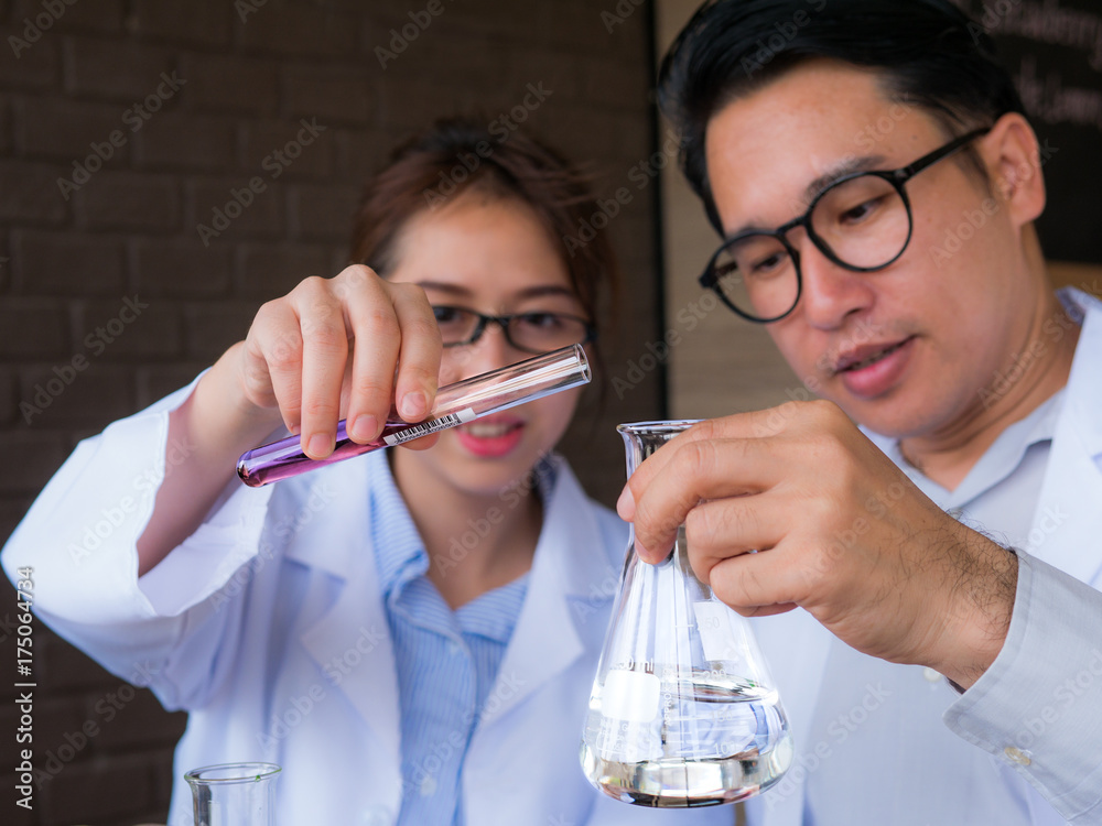 The acting setup of laboratory work. Two Asian young scientists, male and female, are working in the laboratory with the color liquid in the glassware. Selective focused The acting setup of laboratory work. Two Asian young scientists, male and female, are working in the laboratory with the color liquid in the glassware. Selective focused
