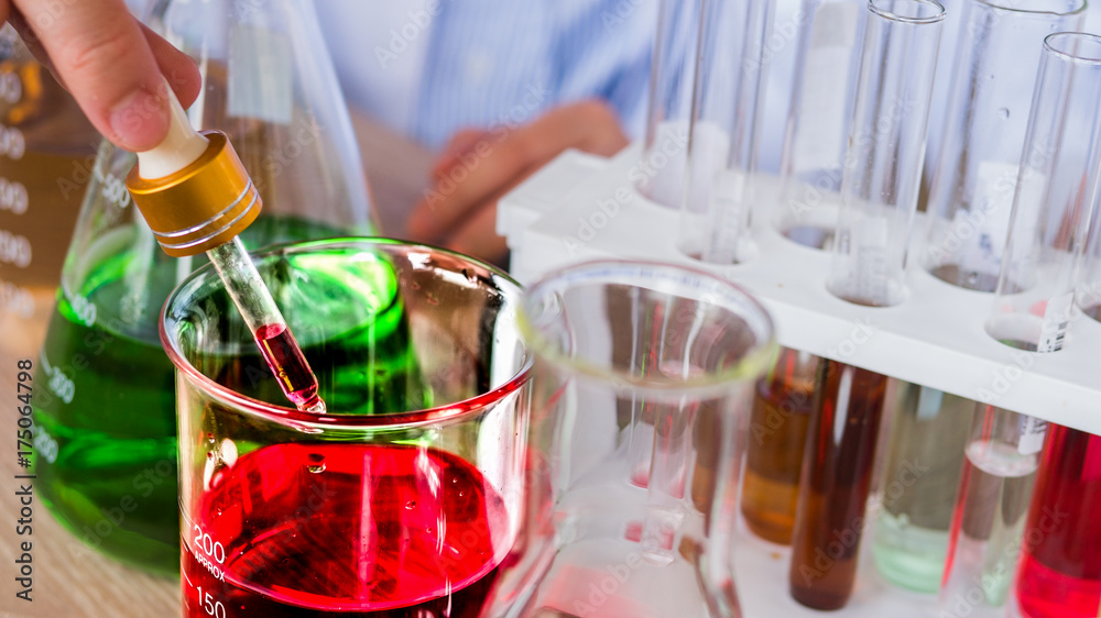The acting setup of laboratory work. Two Asian young scientists, male and female, are working in the laboratory with the color liquid in the glassware. Selective focused