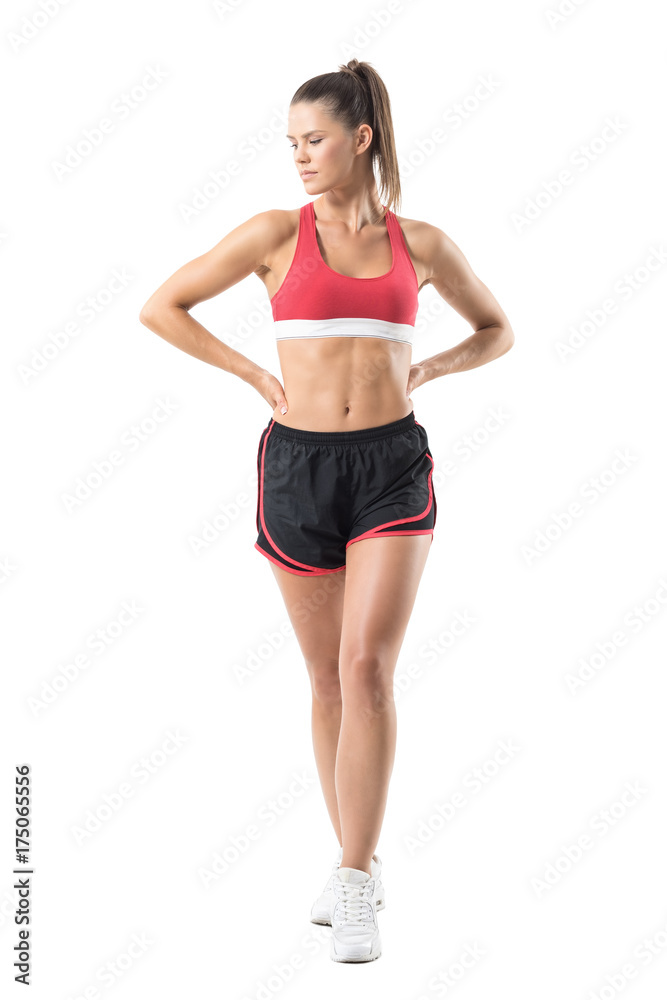 Serious confident fitness female model with hands on hips looking down. Full body length portrait isolated on white studio background. Serious confident fitness female model with hands on hips looking down. Full body length portrait isolated on white studio background.