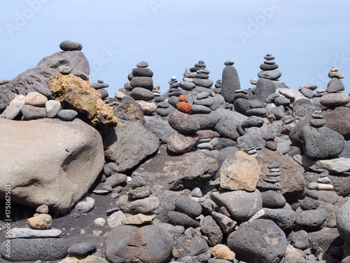 stacks and towers of pebbles and rocks against a blue summer sky