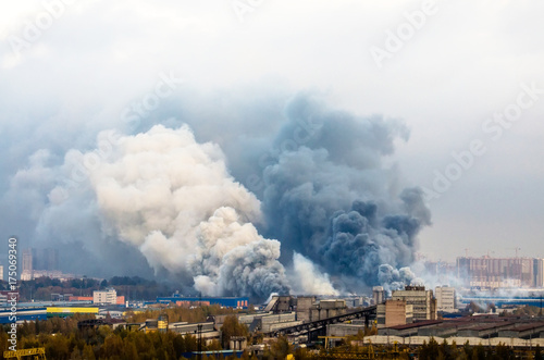 Fire in warehouses with dark and white huge smoke clouds.