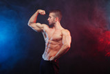 Muscled man model posing on dramatic smoky background. Sports, bodybuilding, healthy lifestyle concept