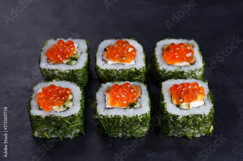 Japanese food, sushi restaurant. Delicious sushi rolls topped with caviar in chopped dill served on black slate with free space for text design