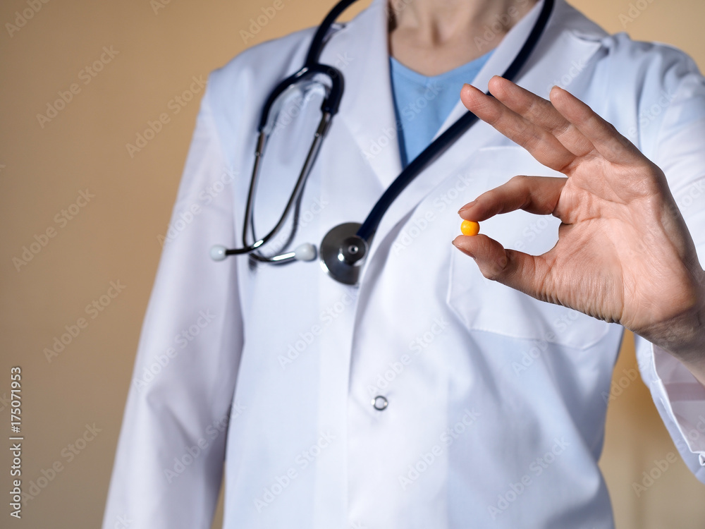A female doctor with a stethoscope on a beige background holds a yellow round tablet. A female doctor with a stethoscope on a beige background holds a yellow round tablet.