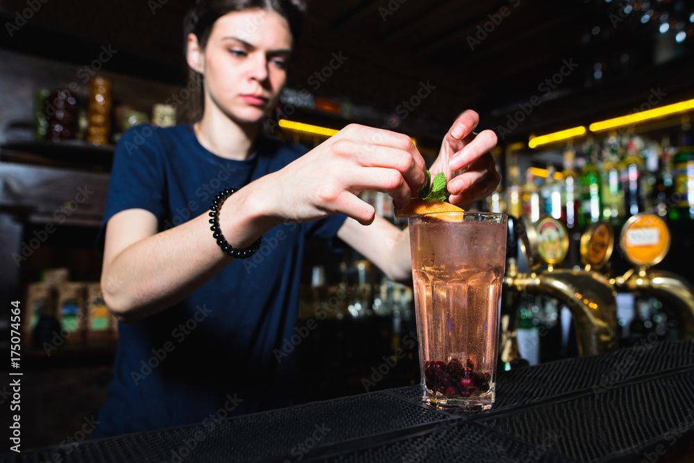 A woman bartender adorns a cocktail at the bar. The barman creates a beautiful cocktail.