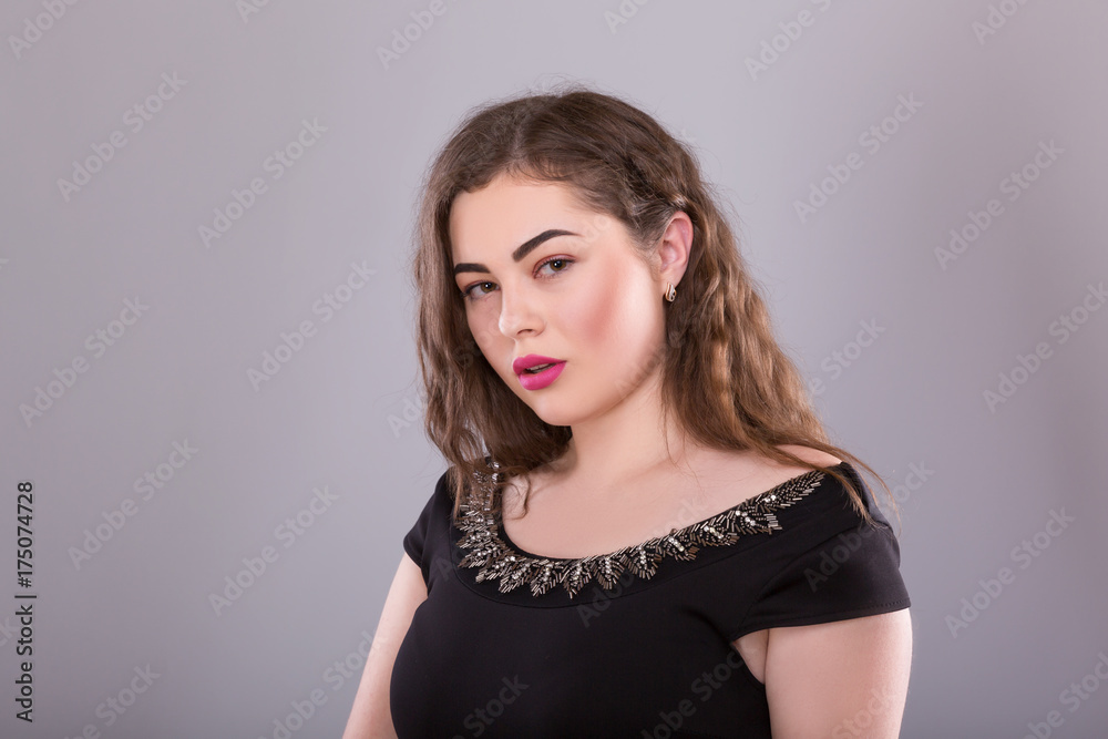Portrait of a plus size female model posing in black dress over grey background. Portrait of a plus size female model posing in black dress over grey background.