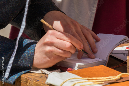 Close up of hands of scribe practicing traditional illumination writing calligraphy with feather quill and ink