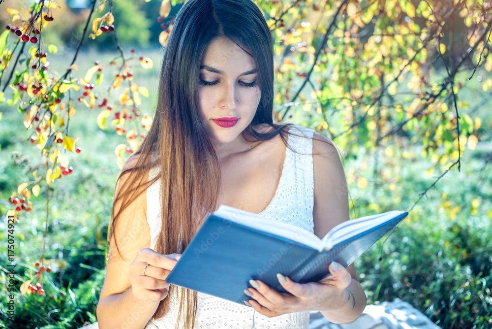 Obraz premium Woman reading an interesting book sitting in a Park on a green lawn on a Sunny summer day. Concept of student education
