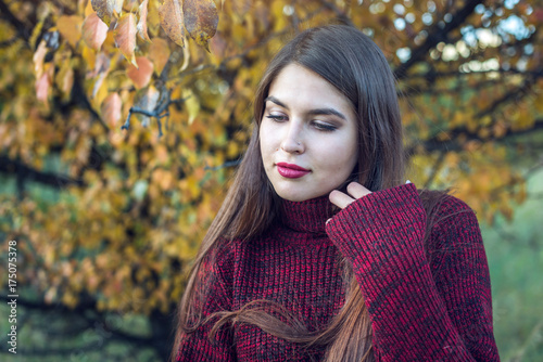 Beautiful colorful portrait of a woman in a red sweater and bright lipstick in the autumn Park. Concept of Autumn mood