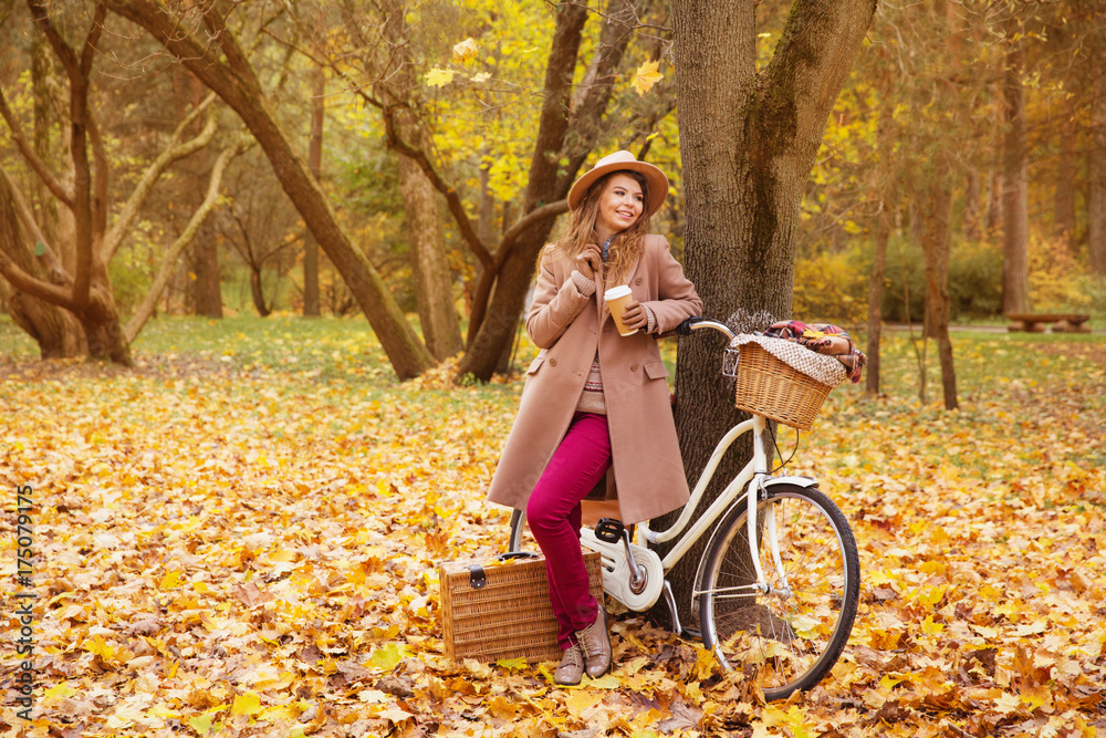 travel concept young woman walk with bicycle picnic set hot drinks in bright autumn city park background copy space  - obrazy, fototapety, plakaty 