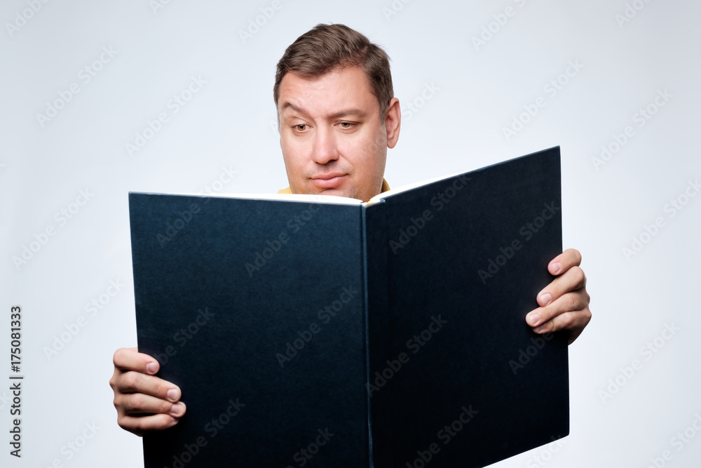 Caucasian man opening big book and with doubt looking in search of important information Caucasian man opening big book and with doubt looking in search of important information