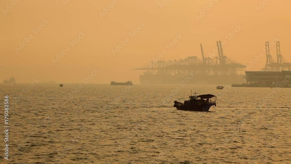 Traditional Chinese fishing boats sailing at sea with large modern Shenzhen port with container ship and cranes in background, back-lit by sunset light; Guangdong province, People's republic of China;