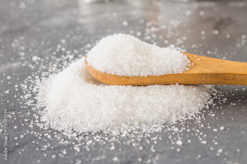 A pile of white sugar sand with a wooden spoon on a dark background.