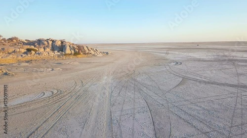 Low flight over the edge of island on large salt pan covered by tracks