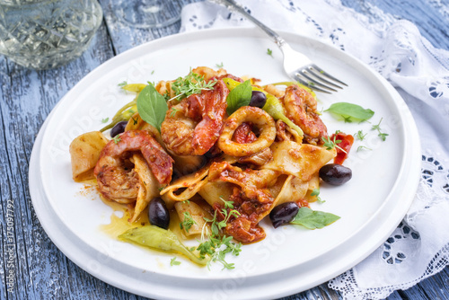 Italian tagliatelle con gamberi e calamari in salsa di pomodoro with olives and peperoni as close-up on a plate