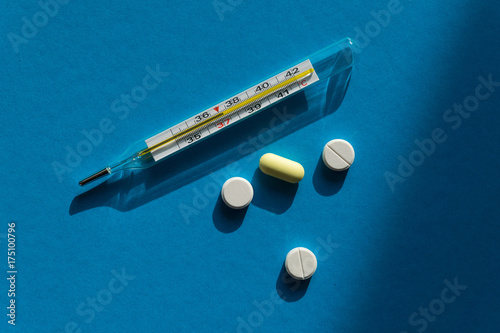 Mercury thermometer and pills against the flu on a blue background