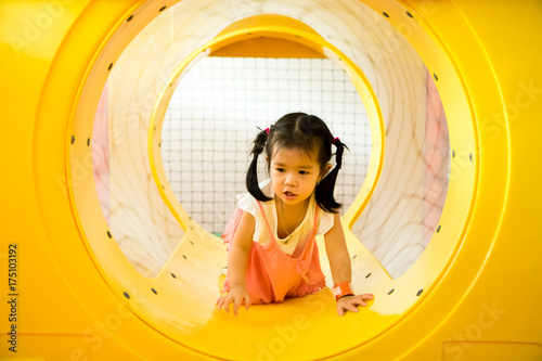 A little smile girl is crawling out of yellow tunnel at playground