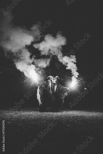 krampus with burning bengal light on a meadow