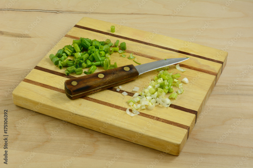 Chopped green onion scallions with green and white parts kept separate on cutting board with knife Chopped green onion scallions with green and white parts kept separate on cutting board with knife