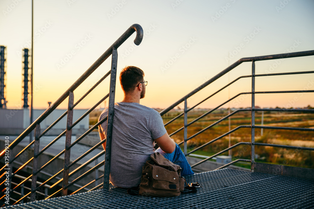 man sitting on the stairs and looking on sunset
