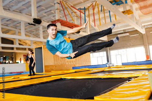 Happy emotional man jumping and flying in trampoline sport center indoors