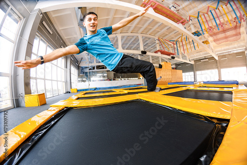 Happy emotional man jumping and flying in trampoline sport center indoors