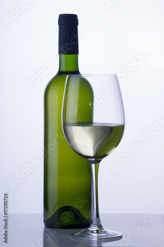 High glass with still white wine and green wine bottle
