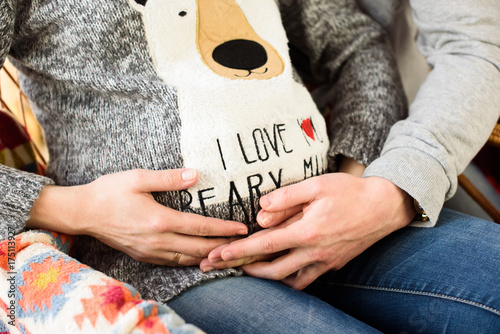 Beautiful pregnant couple in love on the background of a Christmas tree, having a rest on Christmas holidays before the new year. Big pregnant belly