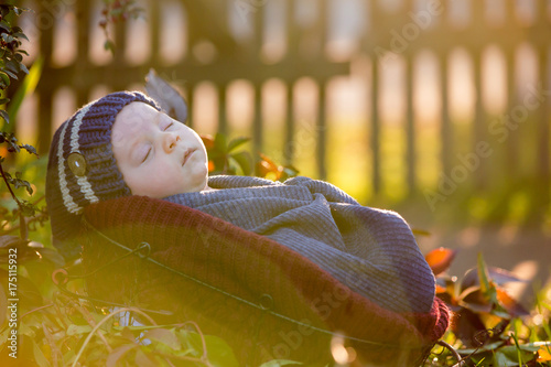 Little newborn baby boy, wrapped in scarf, lying in basket in forest