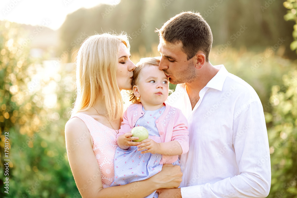 Happy young family spending time together in green nature park. wife with husband and little baby. Mother and father kissing baby Happy young family spending time together in green nature park. wife with husband and little baby. Mother and father kissing baby