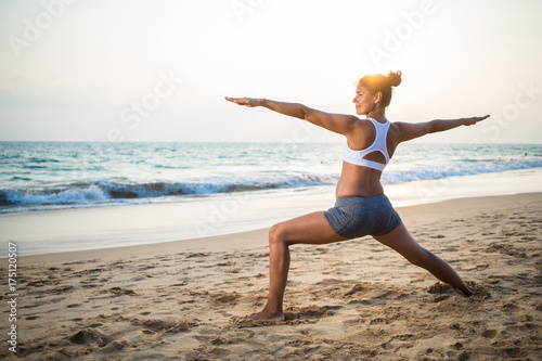 Natural looking pregnant woman practicing yoga at the seashore at sunset