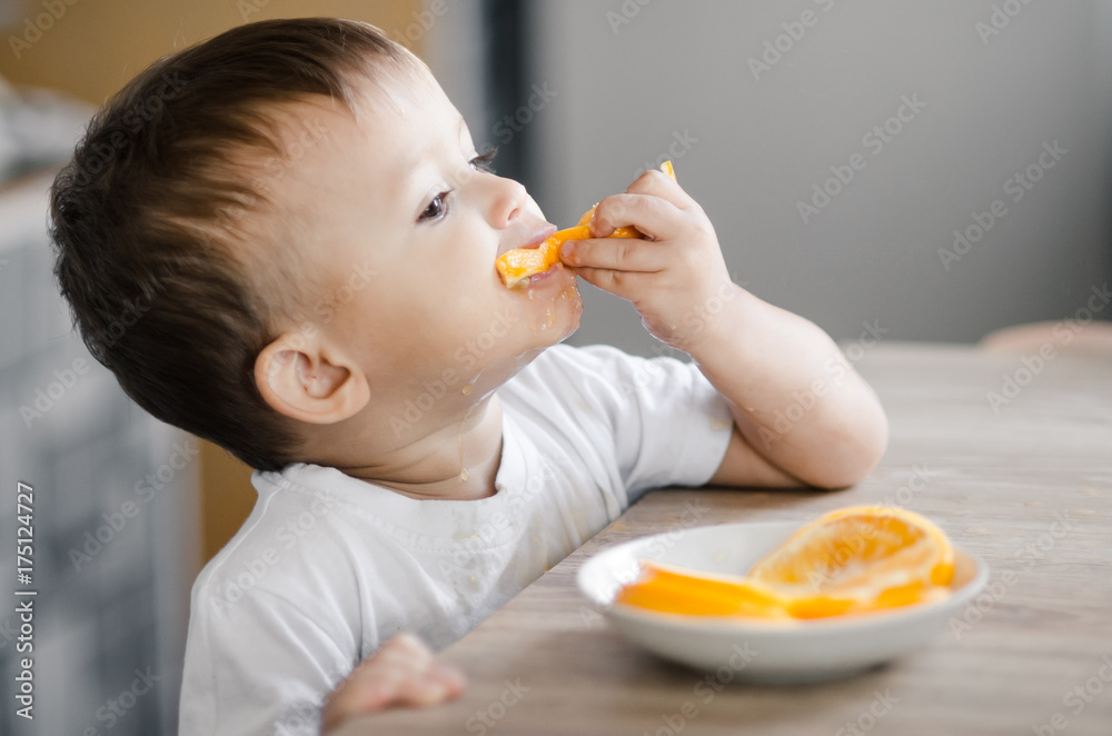 The child in the kitchen eating an orange The child in the kitchen eating an orange