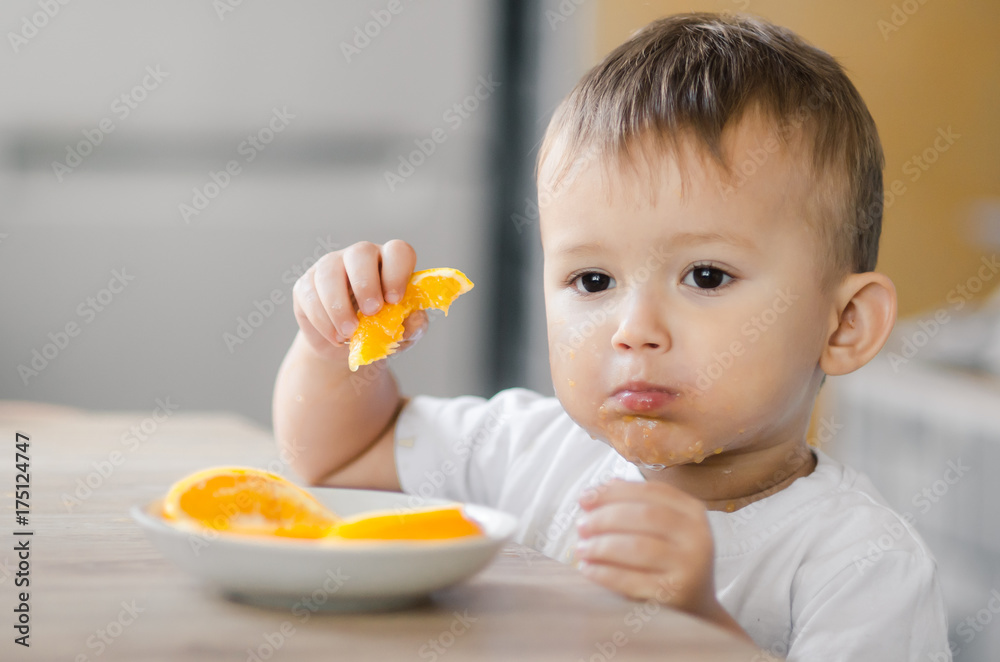 The child in the kitchen eating an orange The child in the kitchen eating an orange