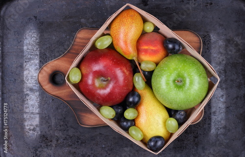 Fototapeta Naklejka Na Ścianę i Meble -  Red apple, dark blue grapes, green apple, yellow pear, green grapes, orange peach in a wooden box on a metallic background in retro style
