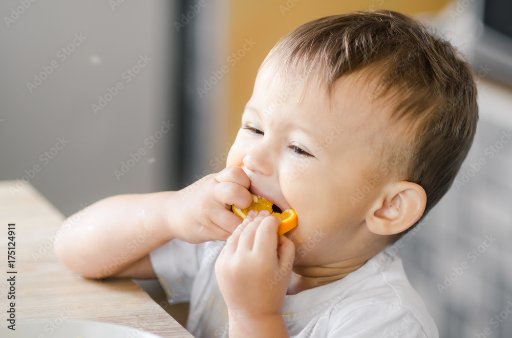 The child in the kitchen eating an orange The child in the kitchen eating an orange