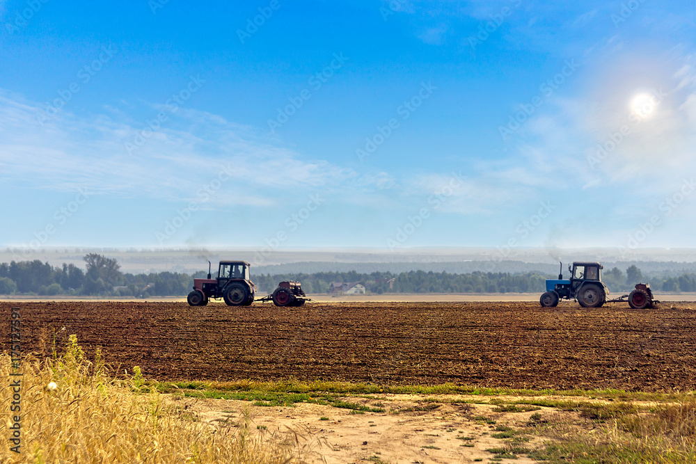 Obraz premium Beautiful agricultural landscape with two old tractors equipped with seeders. Farmers sowing winter wheat in autumn.