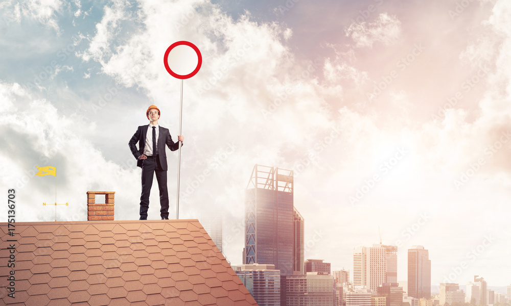 Caucasian businessman on brick house roof showing stop road sign Caucasian businessman on brick house roof showing stop road sign