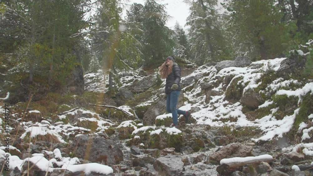 Slow motion shot of girl hiking in trekking boots in the mountain pine forest, dark gray sky, autumn or winter. Snow falling on melting stream. Healthy and active lifestyle, vacation concept. Slow motion shot of girl hiking in trekking boots in the mountain pine forest, dark gray sky, autumn or winter. Snow falling on melting stream. Healthy and active lifestyle, vacation concept.