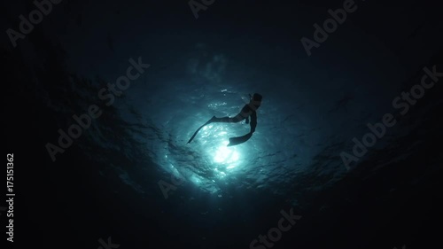 Low angle, scuba diver silhouette swims to surface