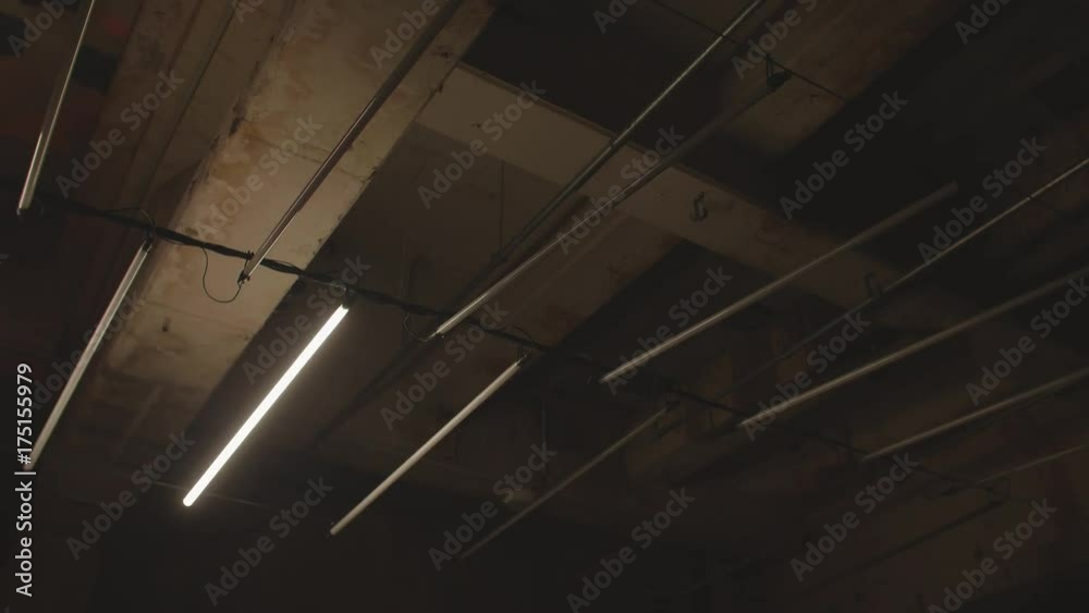 4k shot of white fluorescent lighting turn on and off and in industrial building. Many neon lights blinking and flashing on the ceiling.
