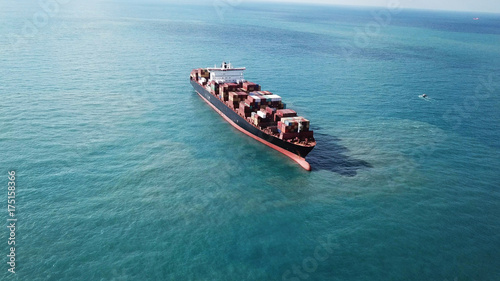 Huge large mega container ship sails on open water fully loaded with containers and cargo - aerial view