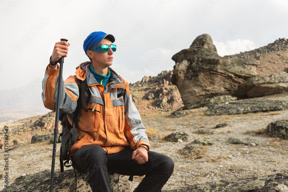 A lonely tourist with a backpack and in sunglasses is resting sitting on a rock