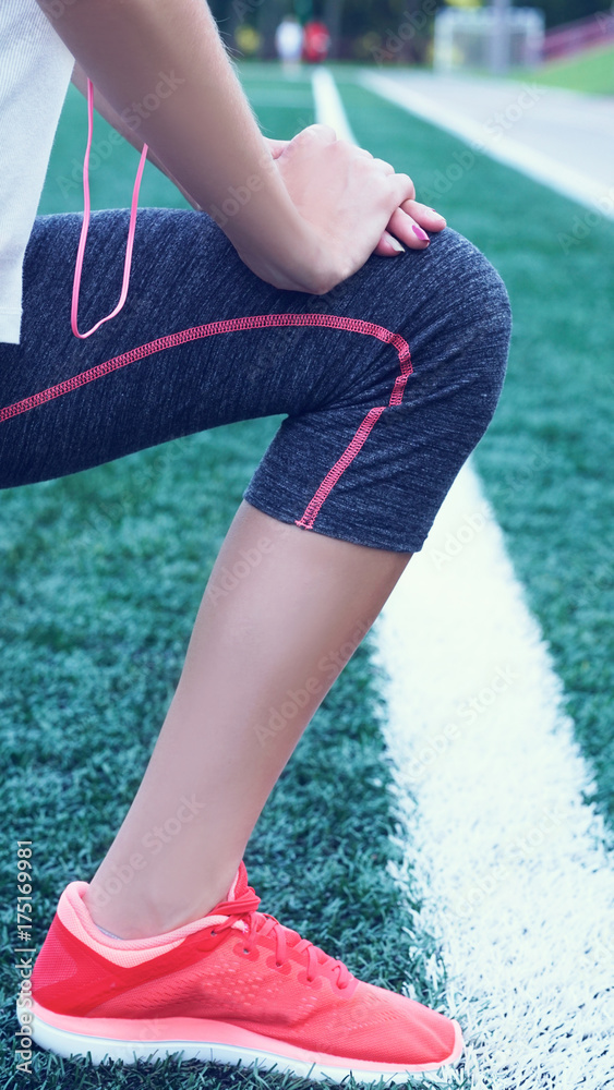 Young fitness girl doing stretching on the stadium. Summer sport activity. Green stadium grass on background.
