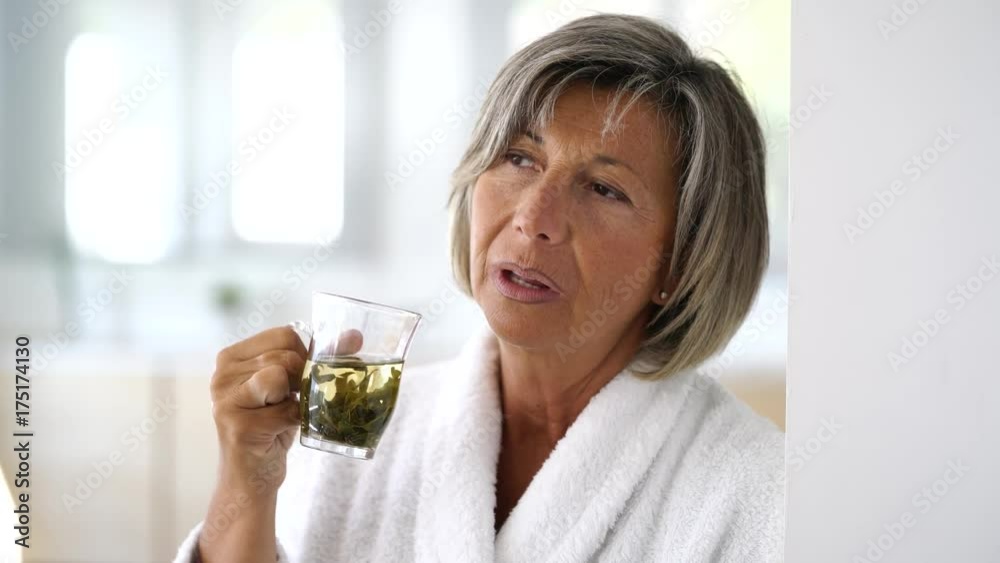 Senior woman in bathrobe drinking hot green tea Senior woman in bathrobe drinking hot green tea