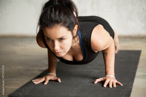 Young attractive woman practicing yoga, doing Push ups, press ups, four limbed staff exercise, chaturanga dandasana pose, working out, wearing black sportswear, indoor close up, studio background