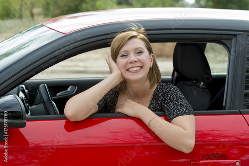 happy attractive woman sitting at driver seat smiling cheerful and proud waving hello from new car © Wordley Calvo Stock