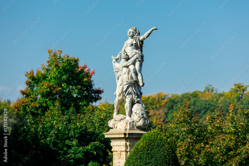 Classic statue in a park with blue sky and tree on background